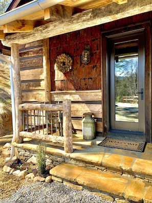 A rustic log cabin with a wooden porch, a stone pathway, and a welcome mat. - Cedar Cliff Cabin at Rivers Edge Rentals. Luxurious reclaimed 125 year old cabin (Waynesville)