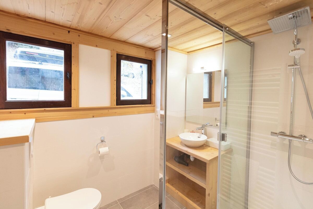 A modern bathroom with a glass shower enclosure, a wooden vanity, and a toilet.