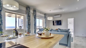 A modern kitchen with a wooden island, large windows, and a blue sofa in the living area. - Premium w terrace. 2 min 2 beach, 90 sqm, Algarve (Quarteira)
