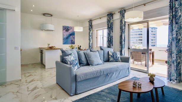 A modern living room with a grey sofa, a coffee table, and a dining area with a table and chairs. - Premium w terrace. 2 min 2 beach, 90 sqm, Algarve (Quarteira)