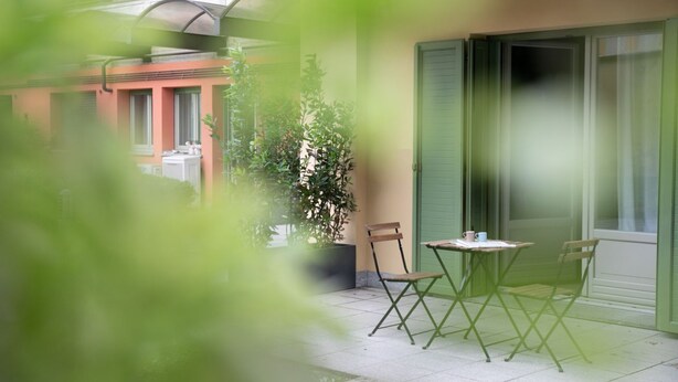 Ein Balkon mit zwei Stühlen, einem Tisch, einer Topfpflanze und einem Gebäude im Hintergrund.