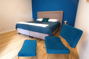 Un dormitorio con una cama, dos sillas azules y una mesita de noche.