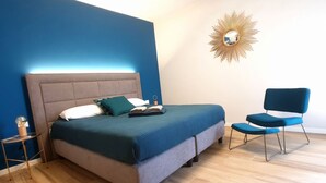 Ein Schlafzimmer mit Bett, Nachttisch, Stuhl und einem an der Wand befestigten Spiegel.