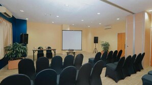 A conference room with rows of chairs, a projector screen, a table with a speaker, and a potted plant. - Arte Yogyakarta (Yogyakarta)