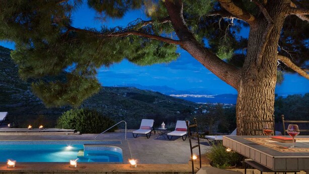 A poolside area with lounge chairs and a table, overlooking a scenic view of a coastal town at dusk.