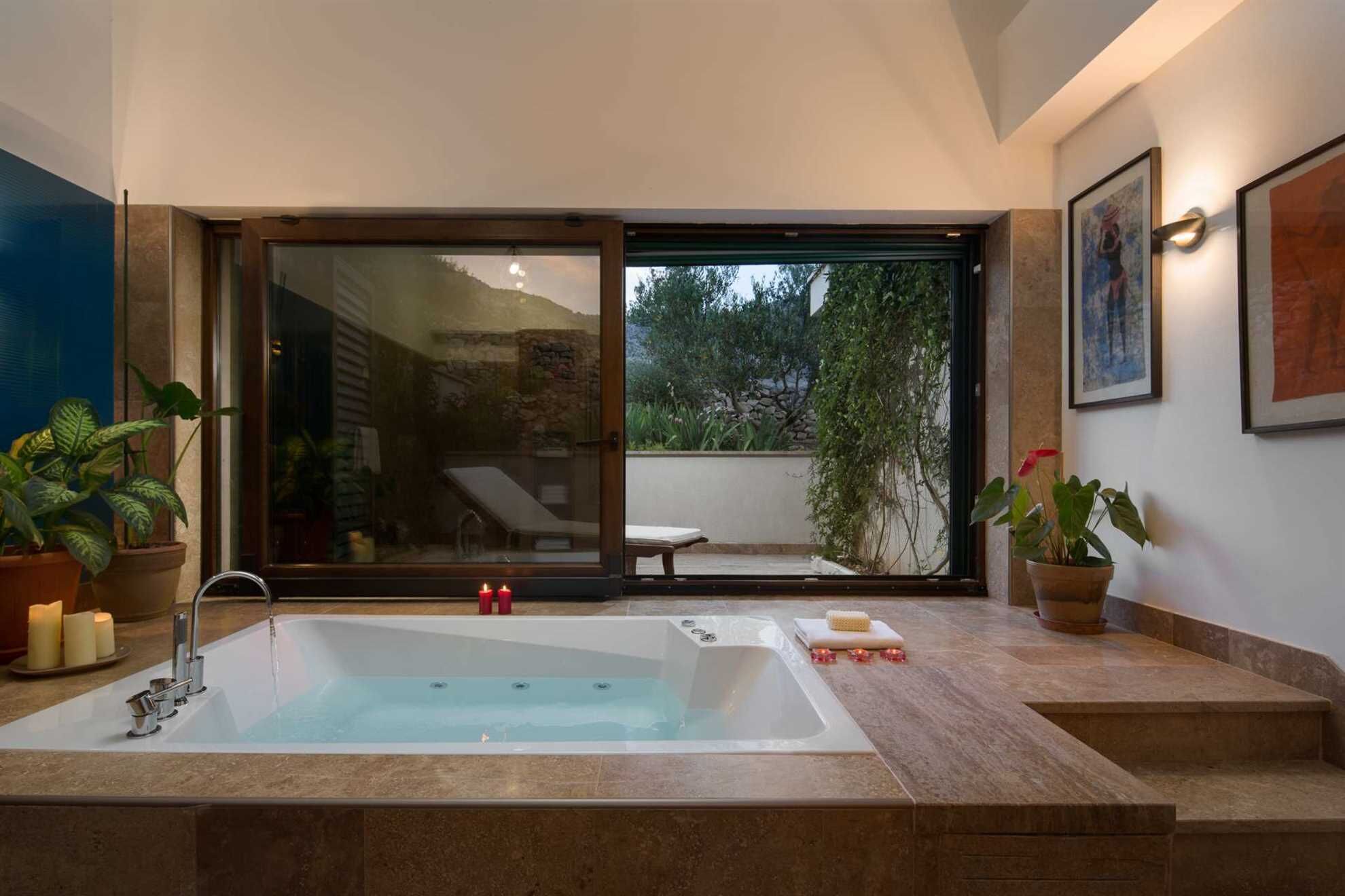 Une salle de bain moderne avec une grande baignoire, une porte vitrée donnant sur un balcon et des plantes en pot.