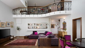 A spacious living room with a curved staircase, a flat-screen TV, a sofa, and a dining area with chairs.