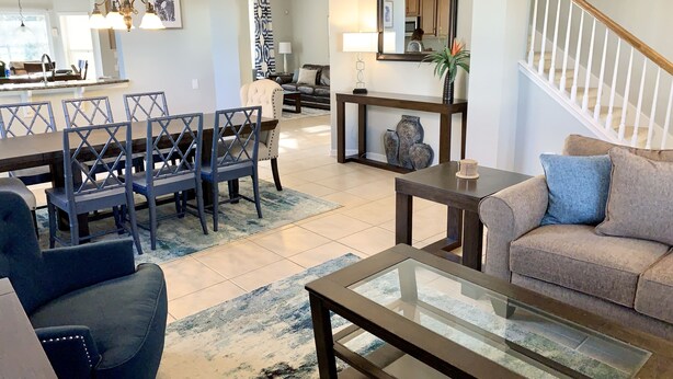 Un salón amplio con comedor, una escalera y una cocina al fondo.