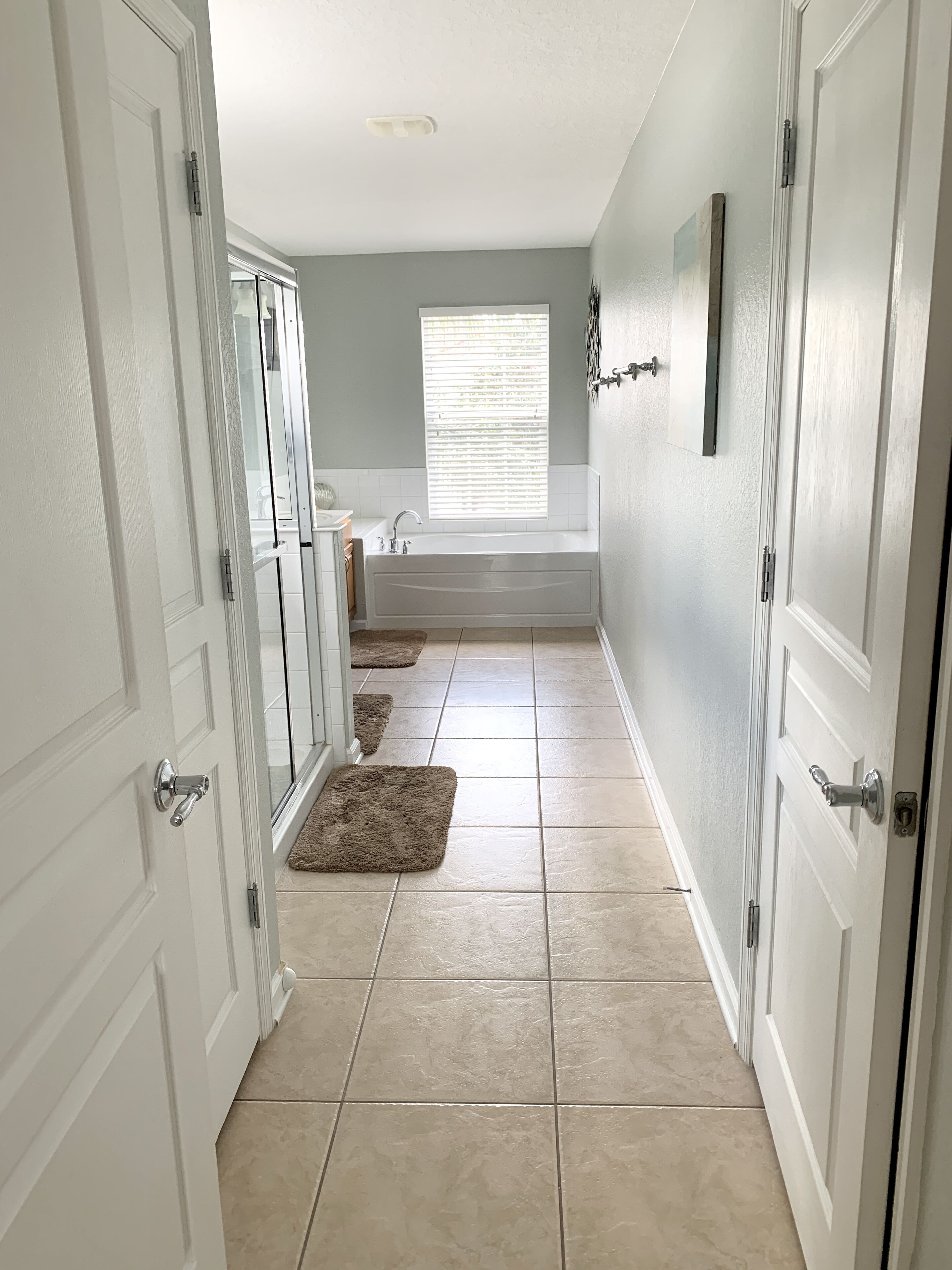 A hallway with a bathtub, a window with blinds, and a door with a handle.