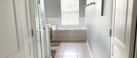 A hallway with a bathtub, a window with blinds, and a door with a handle.