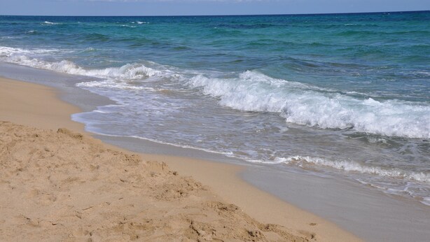 A beach with clear blue water and a sandy shore.