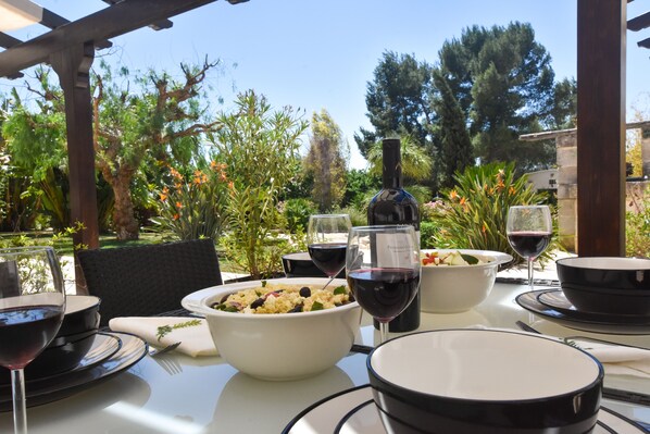 An outdoor dining area with a table set for a meal, surrounded by greenery and trees.