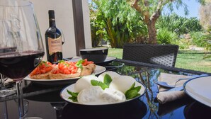 Una mesa dispuesta con una botella de vino, una copa de vino tinto, una fuente de bruschetta y una fuente de mozzarella.