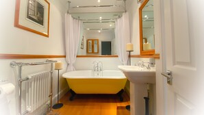 Une salle de bain avec une baignoire, un lavabo, des toilettes, un radiateur et un tableau encadré au mur.