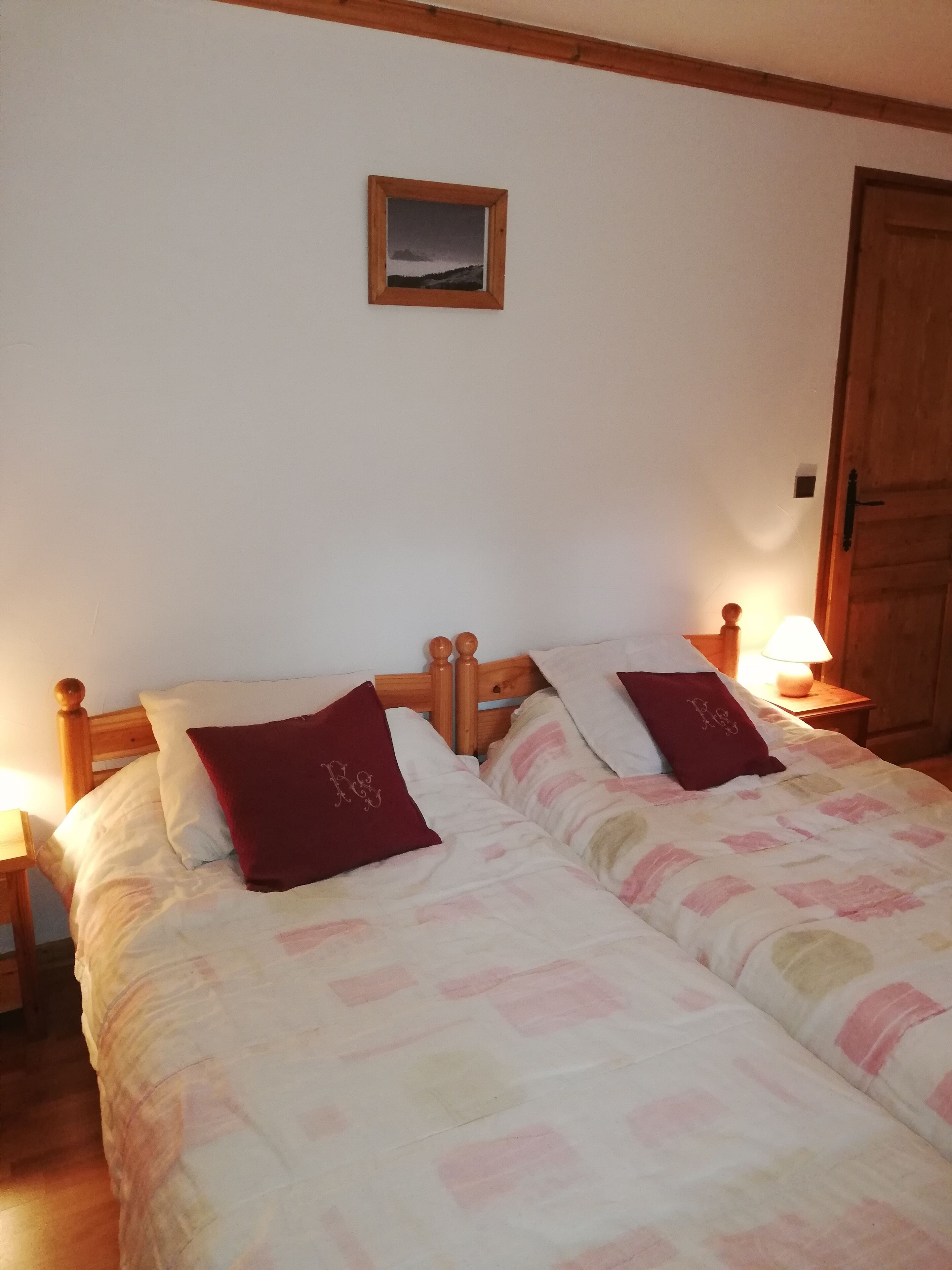 Un lit double avec deux oreillers, une table de chevet avec une lampe et un tableau encadré au mur.