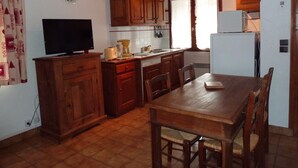 A kitchen with wooden cabinets, a dining table, chairs, a refrigerator, a coffee maker, a toaster, and a clock on the wall.