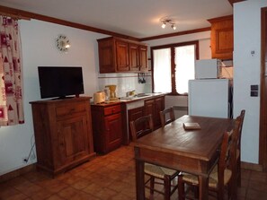 Uma cozinha com armários de madeira, uma mesa de jantar, cadeiras, uma geladeira, uma cafeteira, uma torradeira e um relógio na parede.