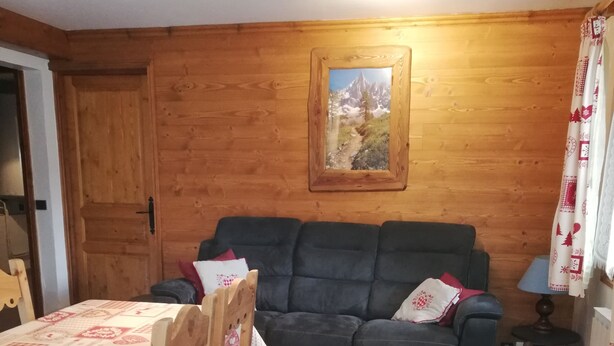 A cozy room with a wooden wall, a sofa, a dining table with chairs, and a small table with a lamp.
