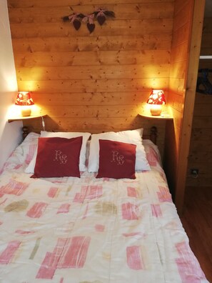 Quarto com painéis de madeira, uma cama, duas luminárias de apoio e um raminho de corações decorativos.