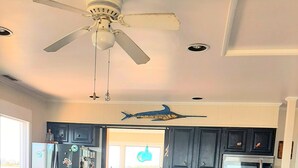 Eine moderne Küche mit dunklen Schränken, einem Edelstahlkühlschrank, einer Mikrowelle und einem Backofen. Im Wohnbereich befindet sich ein blaues Sofa mit Zierkissen.