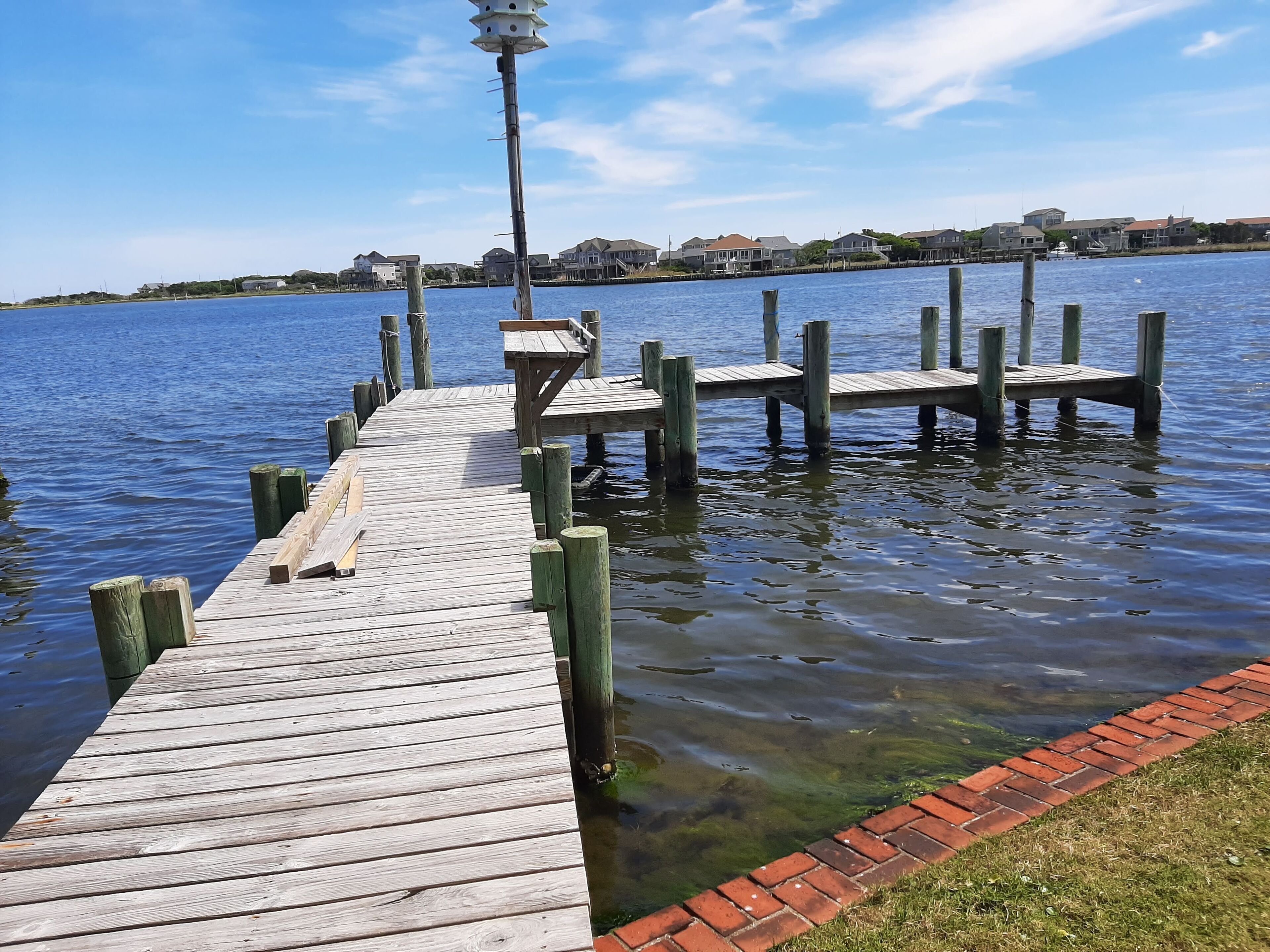 A wooden pier extending into a calm body of water with a clear view of houses in the background.