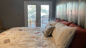 A bedroom with a large bed, a wooden headboard, and a view through a glass door to the outside. - Sunshine & Beach Views at 2046 Beach Blvd (Biloxi)