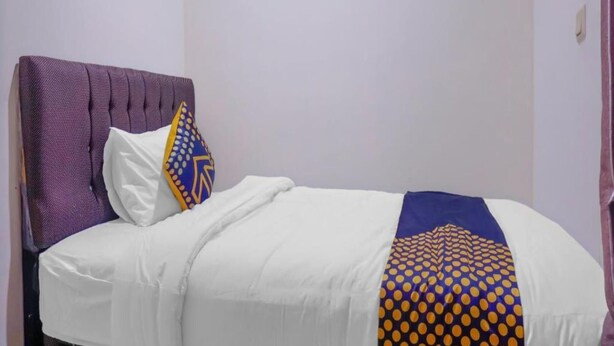A single bed with a white mattress, a purple headboard, and a decorative pillow with a geometric pattern.
