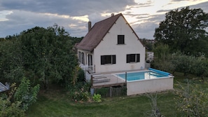 Una casa a due piani con piscina, immersa nel verde e circondata da alberi.