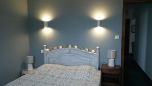 Quarto com cabeceira de madeira, duas luminárias de apoio e cama com colcha estampada.