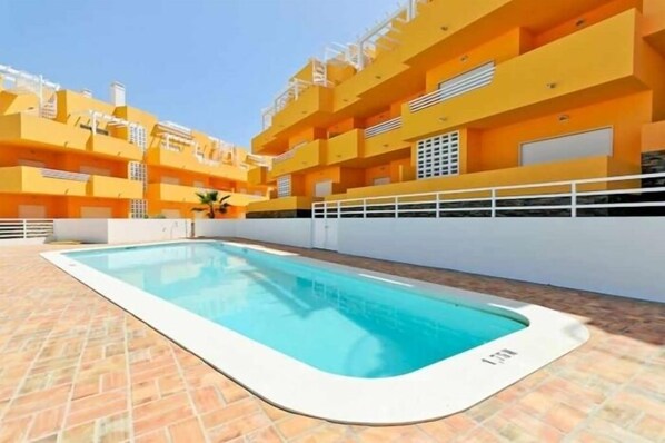 A swimming pool with a tiled deck, surrounded by yellow multi-story buildings with balconies.