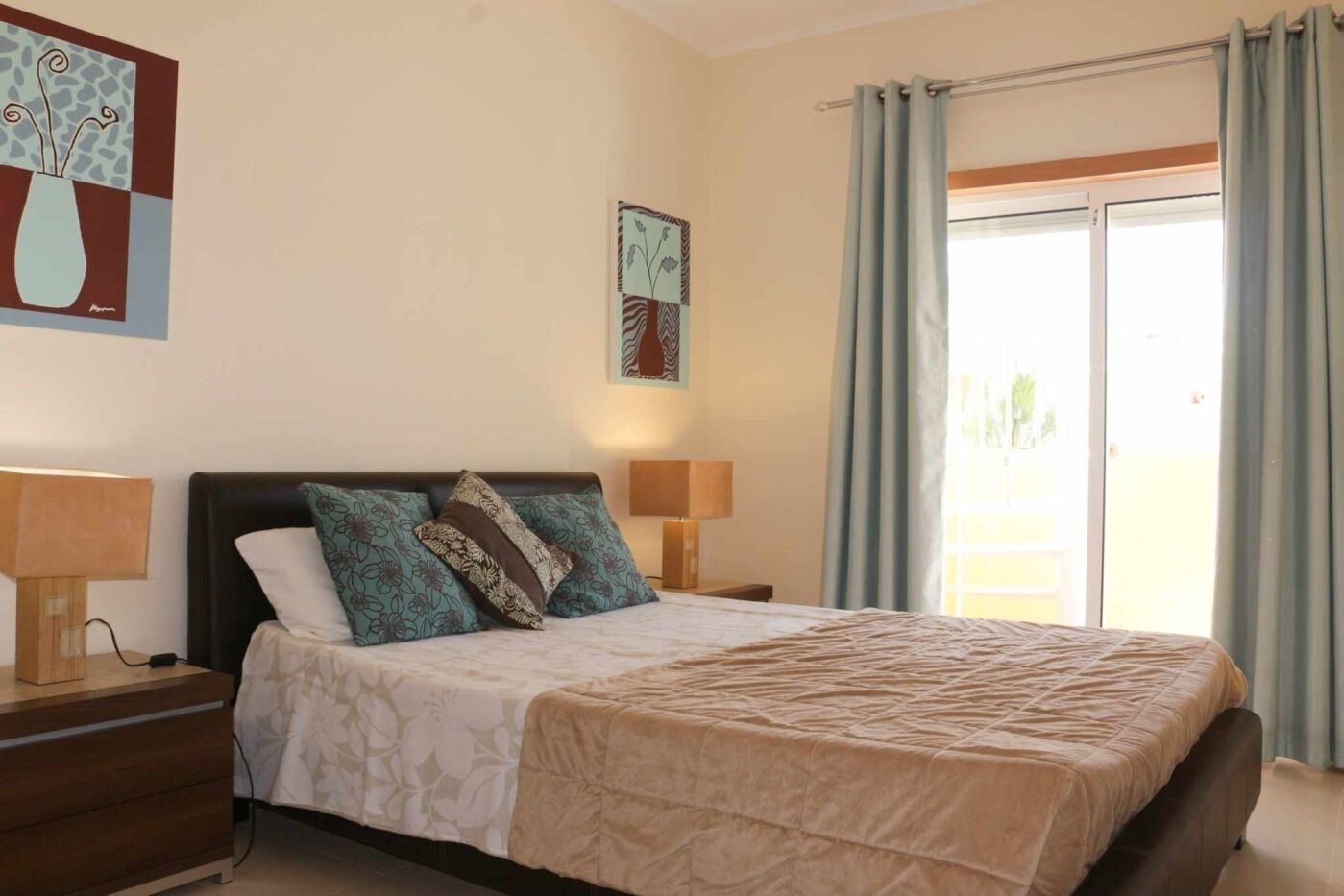 Een slaapkamer met een bed, twee nachtkastjes, gordijnen voor het raam en kunstwerken aan de wanden.