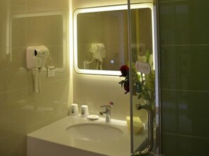 Un baño con lavamanos blanco, espejo, secador de pelo y un florero con una rosa roja.