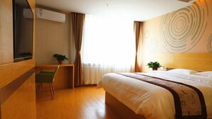 A hotel room with a bed, a desk, a chair, a window with curtains, and a wall with a circular design. - Greentree Inn Business Hotel (Shenyang Huaxiang Shengjing Hospital) (Shenyang)