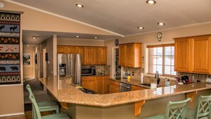 A spacious kitchen with wooden cabinets, granite countertops, stainless steel appliances, and a large island with bar stools. - AC! Beautiful, Cozy Home, Walk to Village Lake (Pagosa Springs)