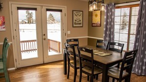 A dining area with a wooden table and chairs, a chandelier, and a view of a snowy landscape through the door. - AC! Beautiful, Cozy Home, Walk to Village Lake (Pagosa Springs)