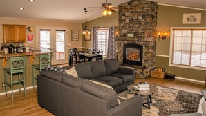A cozy living room with a fireplace, a dining area, and a kitchen with wooden cabinets. - AC! Beautiful, Cozy Home, Walk to Village Lake (Pagosa Springs)