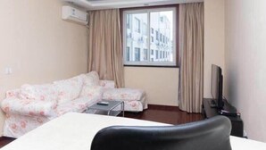 A hotel room with a sofa, a small table, a TV, and a window with curtains.