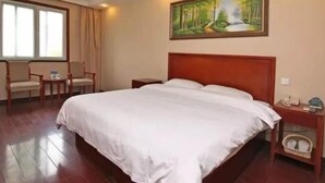 A hotel room with a large bed, a nightstand, a chair, a painting of a forest scene, and a window with curtains.