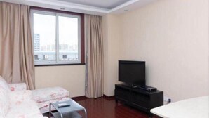 A hotel room with a bed, a TV on a black stand, a small table, and a window with curtains.