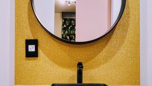 Un baño con un espejo redondo, un lavabo negro y una pared amarilla con textura.