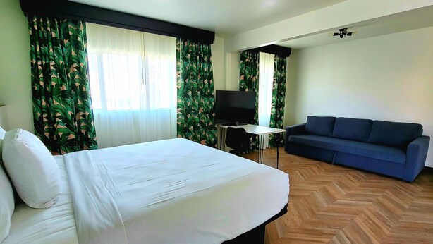 Una habitación de hotel con una cama, un sofá azul, un televisor y una mesita.
