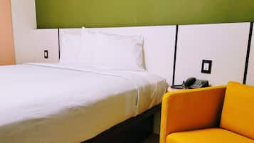 A hotel room with a bed, a yellow chair, a telephone, and a green accent wall.