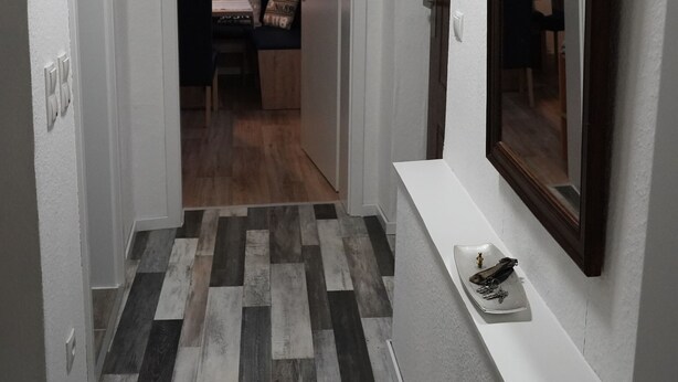 Un couloir avec un sol à carreaux, un miroir au mur et une porte donnant sur une pièce où se trouvent un lit et une carte du monde accrochée au mur.