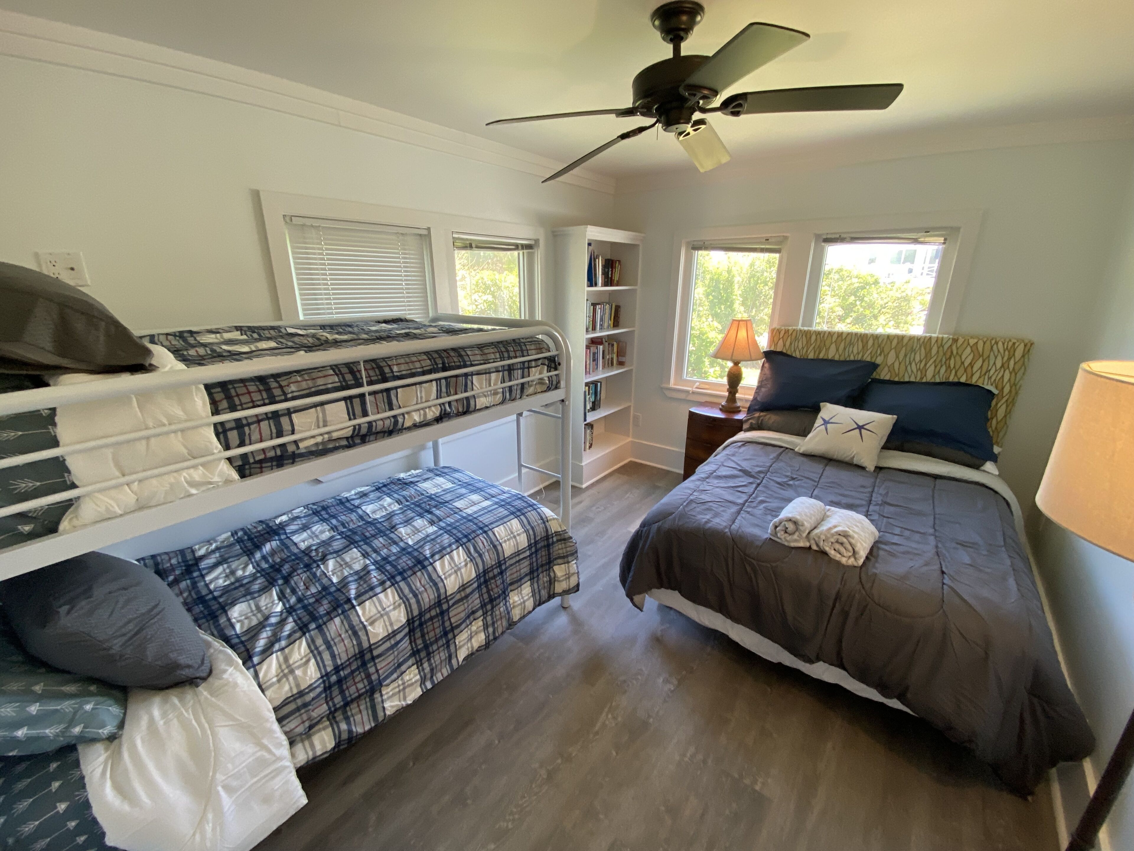 A bedroom with bunk beds, a desk, a bookshelf, and a window with a view of trees.