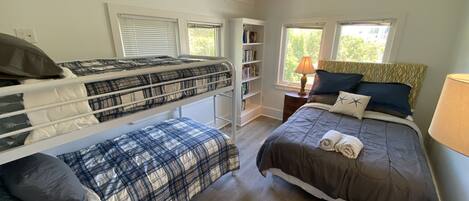 A bedroom with bunk beds, a desk, a bookshelf, and a window with a view of trees.