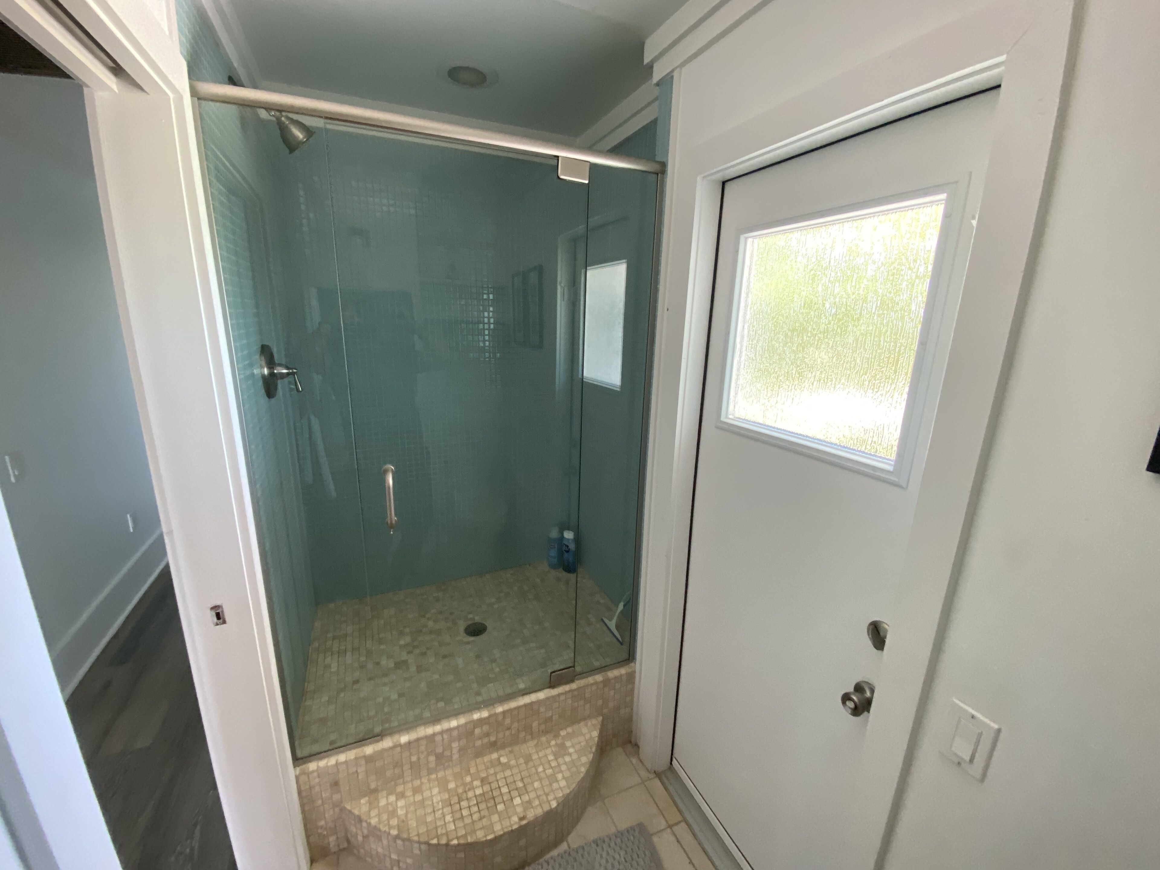 A bathroom with a glass shower enclosure, a small window, and a door with a handle.