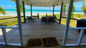A covered outdoor area with a wooden deck, a table with chairs, and a view of the beach and ocean. - Hope Town's Top Rental: Beachfront sunsets, AC, free boat dock, & close to town! (Hope Town)