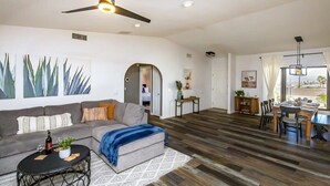 A modern living room with a sofa, coffee table, and a dining area with chairs and a table. - Trendy Getaway + Pool, Spa, Game Room, Views (Lake Havasu City)