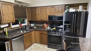 A modern kitchen with wooden cabinets, stainless steel appliances, a built-in microwave, oven, and refrigerator. There is a small dining area with a table and chairs. - Modern House in Wyandotte (Wyandotte)