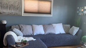 A modern living room with a grey sectional sofa, a wooden coffee table, and a large window with blinds. - Modern House in Wyandotte (Wyandotte)